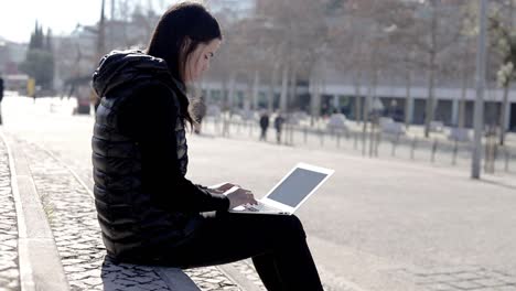Focused-young-woman-using-laptop-on-street